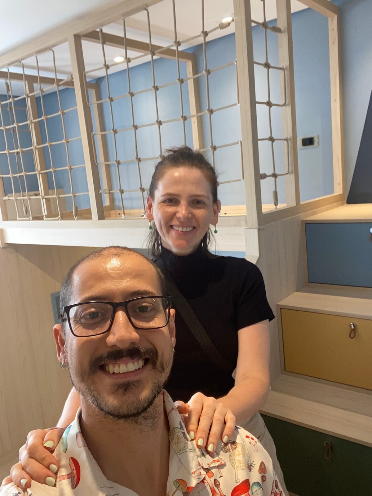 Vinicius e Luana, fundadores da Laço em Fios, sorrindo diante de um mezanino com trama
